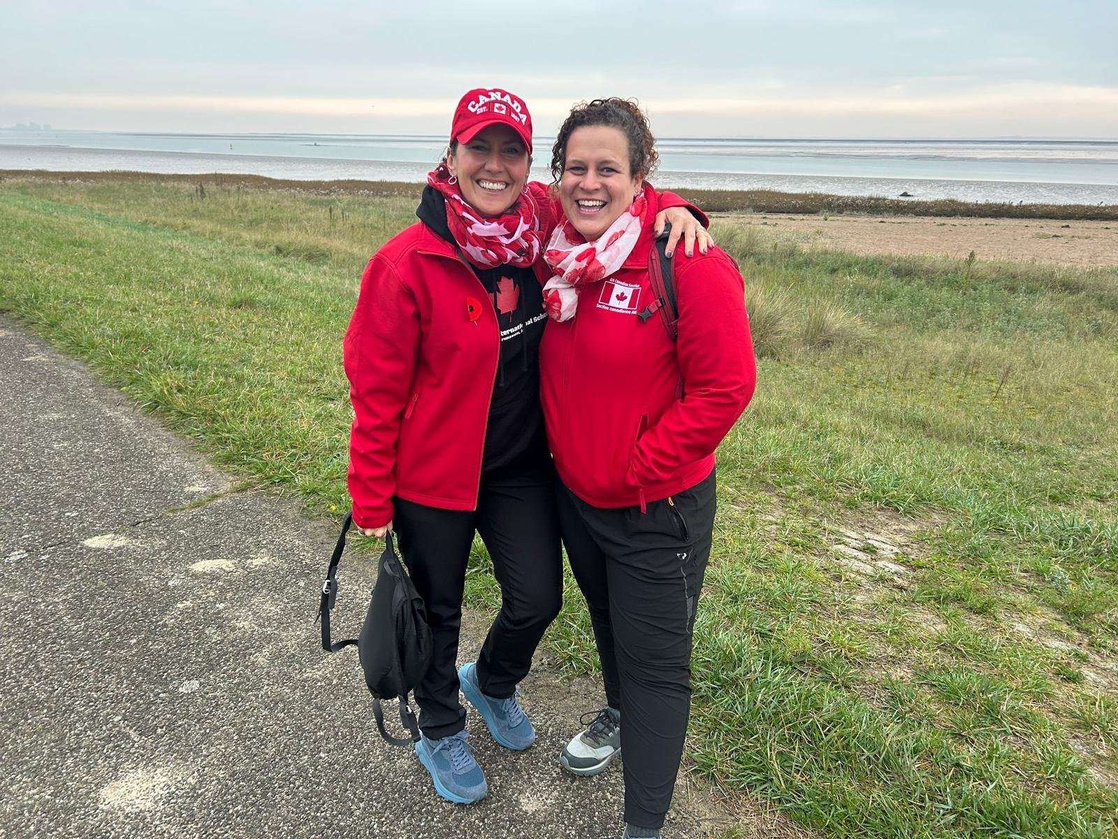 Two women in red jackets and hats standing on a path by water Description automatically generated